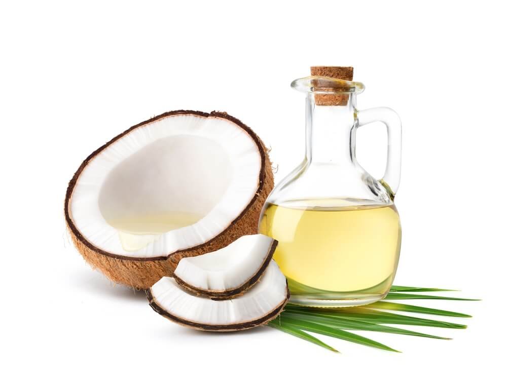 Jar of coconut oil placed next to a whole coconut and coconut flakes, showcasing the natural source of coconut oil for skincare.