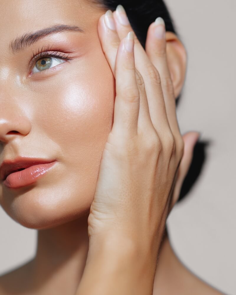 Woman gently touching her face, symbolizing attentiveness and listening to her skin’s needs in a minimalist skincare routine.